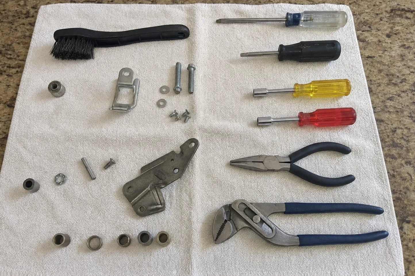 Hand tools laid out on a towel on a stone counter beside a hinge bracket, bushings, bolts and washers